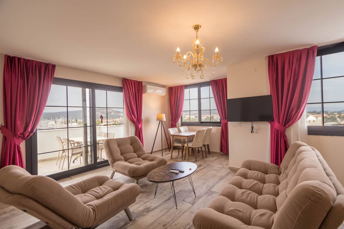 A spacious room with large windows, a chandelier, and a dining area with a table and chairs.