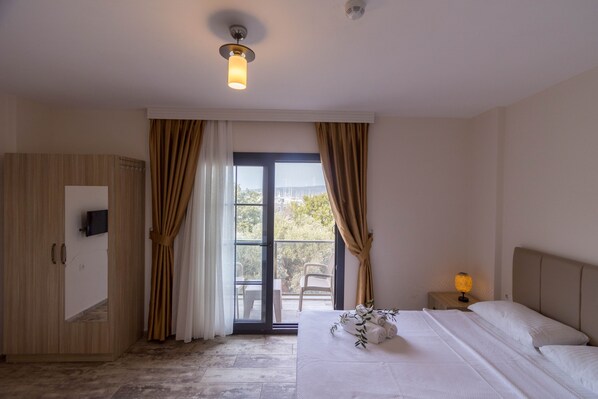 Una habitación de hotel con una cama, una mesita de noche con lámpara, un televisor en la pared y una puerta corrediza a un balcón.