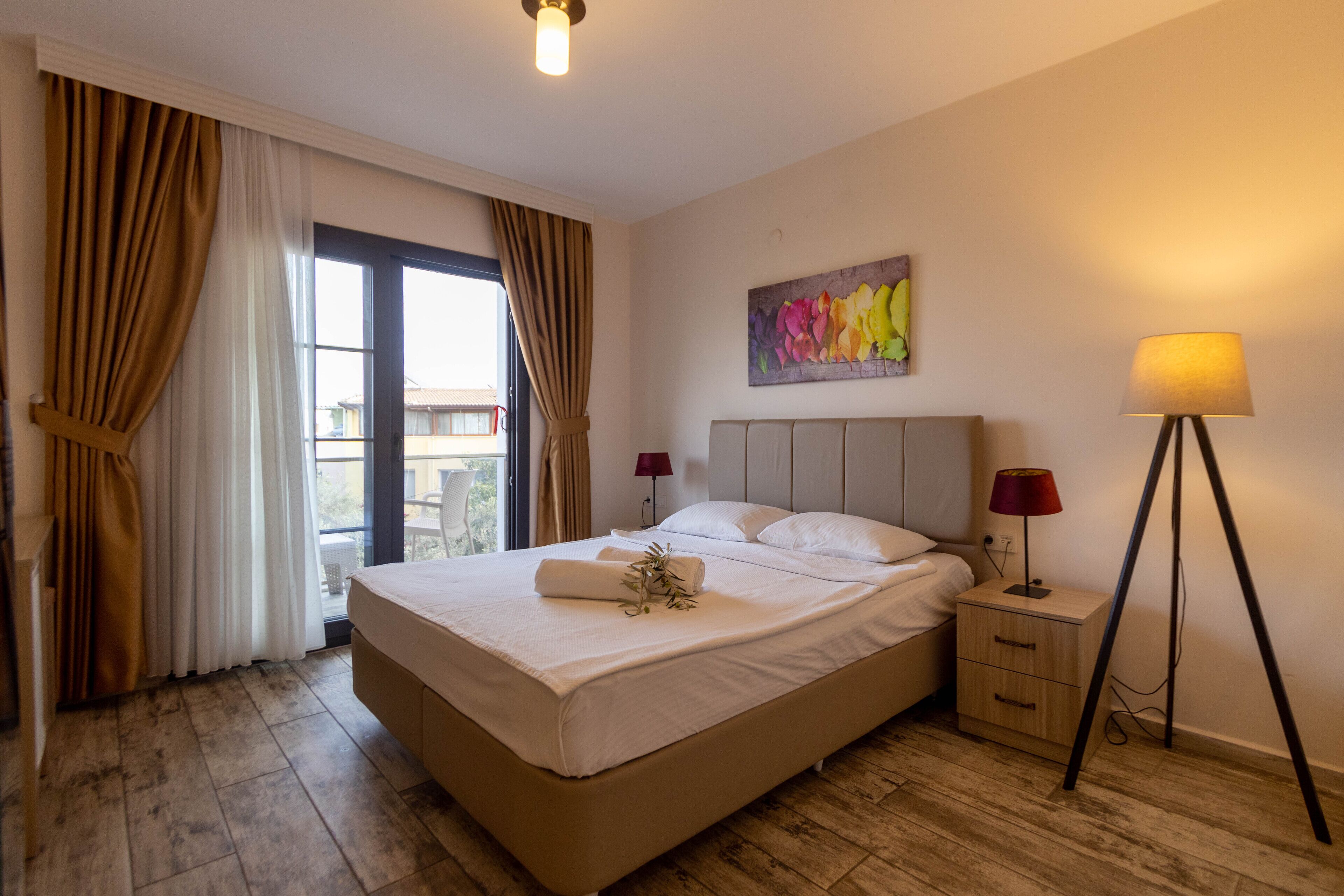 A neatly made bed with a headboard, a bedside table with a lamp, and a window with curtains.