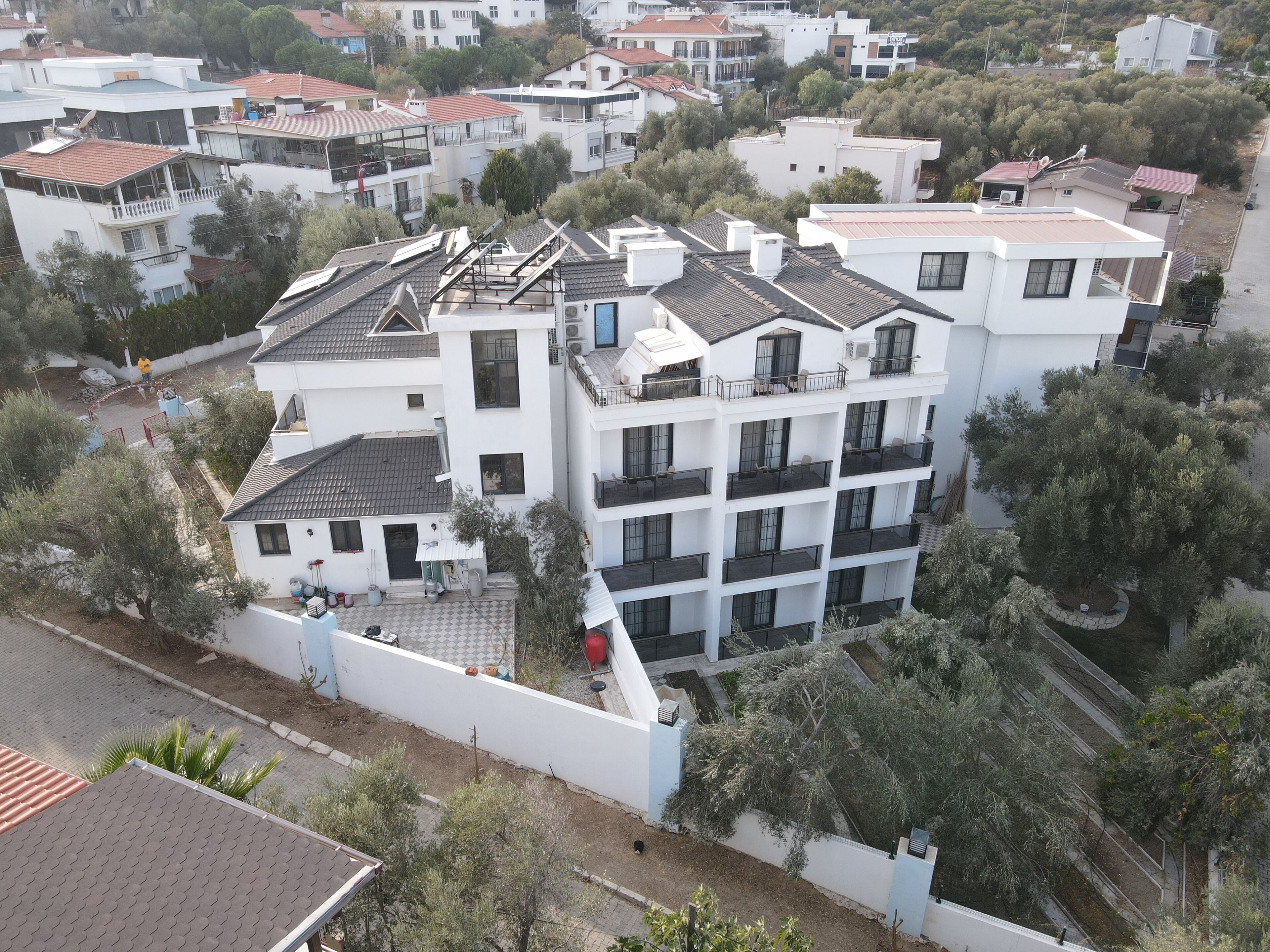 Un immeuble résidentiel à plusieurs étages, doté de balcons, d’un toit recouvert de tuiles et entouré de verdure.