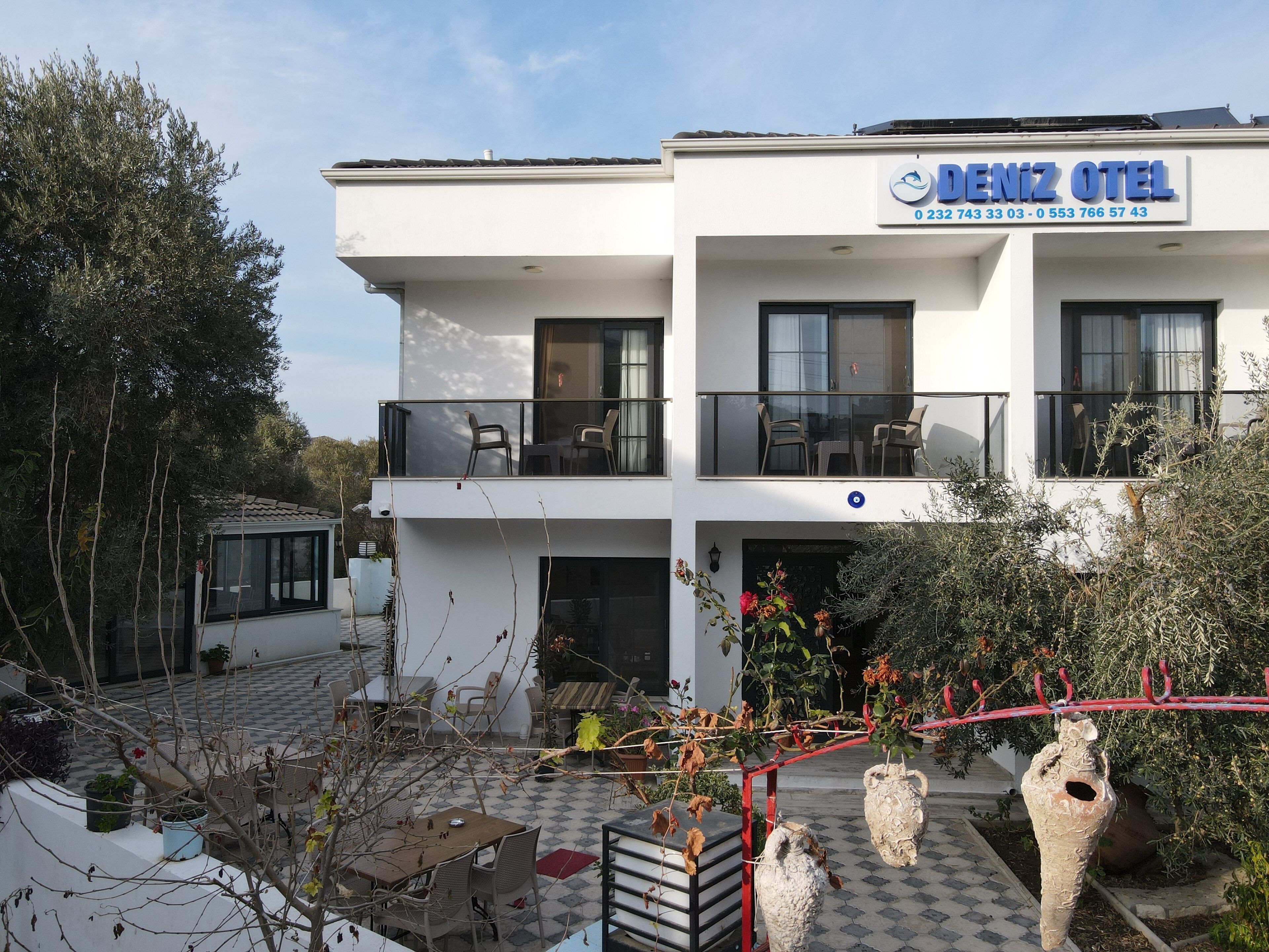 A two-story hotel with a balcony on the upper floor, outdoor seating, and a garden area with potted plants.