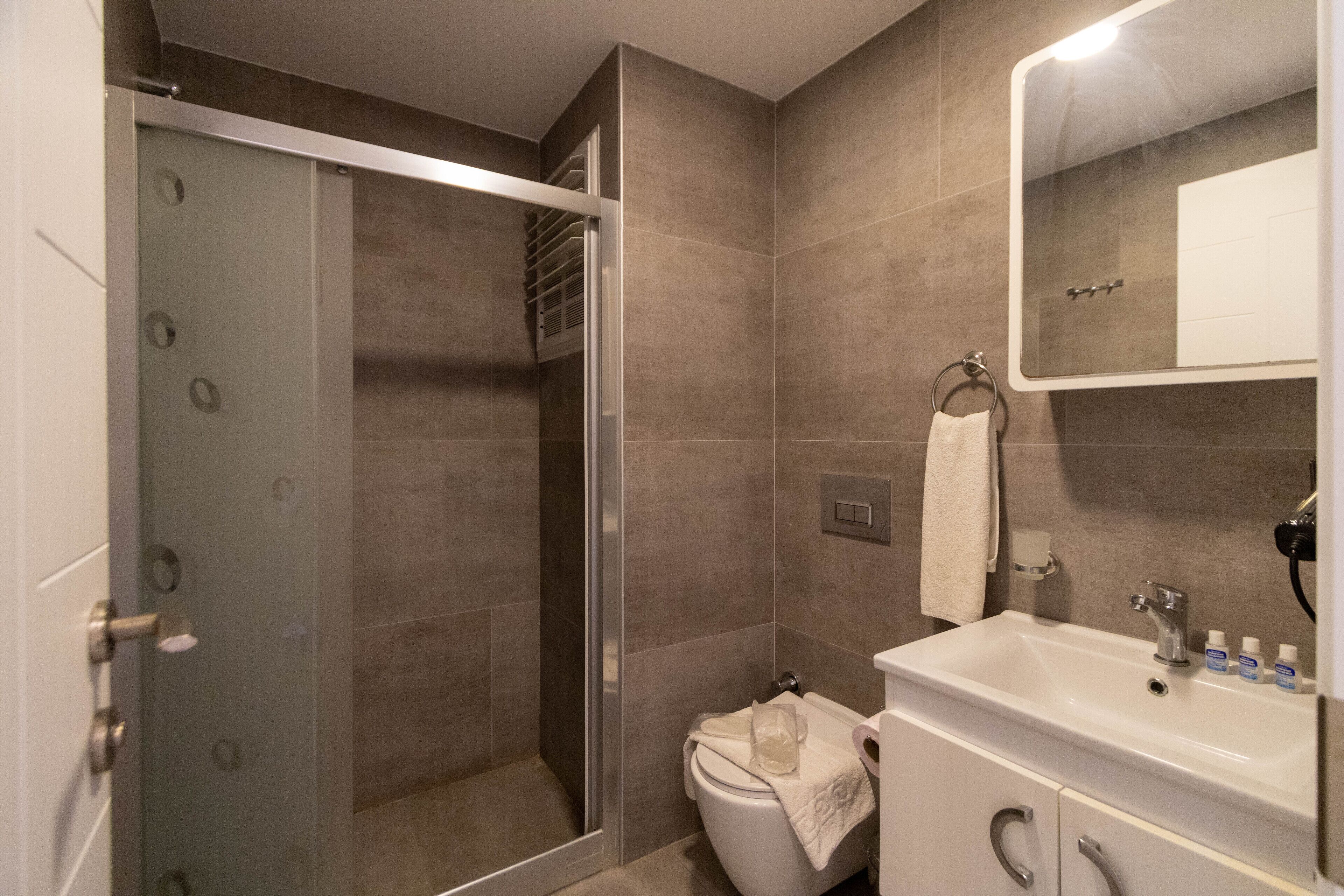 Un baño moderno con cabina de ducha de vidrio, inodoro blanco y lavamanos con artículos de aseo.