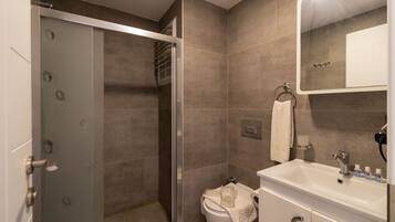 Un baño moderno con cabina de ducha de vidrio, inodoro blanco y lavamanos con artículos de aseo.