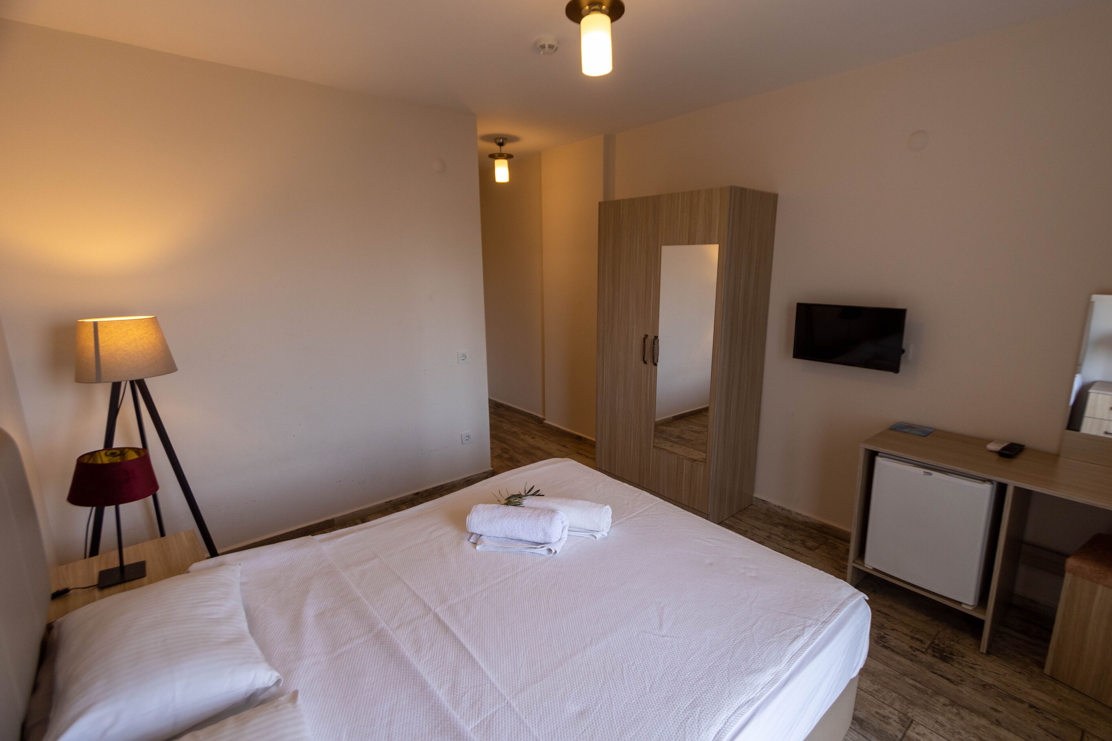 Een hotelkamer met een net opgemaakt bed, een bureau met een televisie en een kleine koelkast.