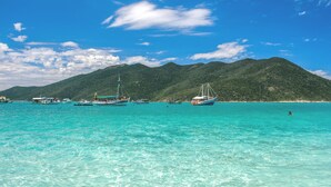 A coastal scene with clear turquoise water, boats, and a mountainous backdrop. - Apartment in the city center (Praia dos Anjos)
