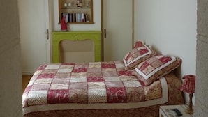 A bedroom with a bed, a small table, a bookshelf, and a fireplace.