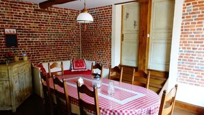 A dining area with a brick wall, wooden chairs, a table with a checkered tablecloth, and a hanging light fixture.