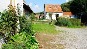 A rural house with a gravel driveway, a fenced garden, and a white building with a tiled roof.