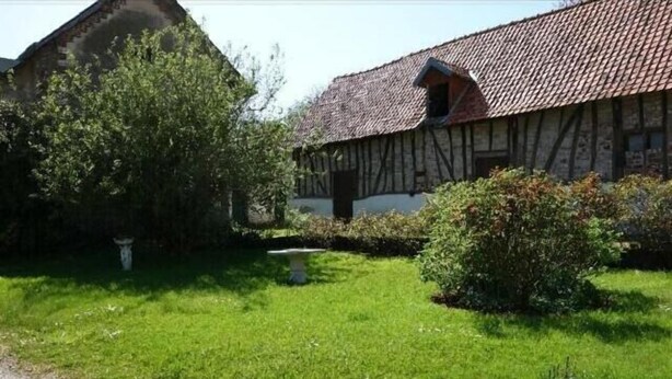 A traditional half-timbered house with a tiled roof, surrounded by a well-maintained garden with a pathway leading to the entrance.