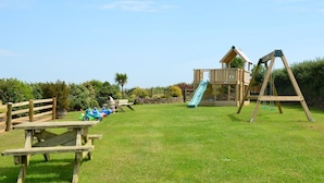 Un parque infantil con tobogán, columpios y mesas de picnic.