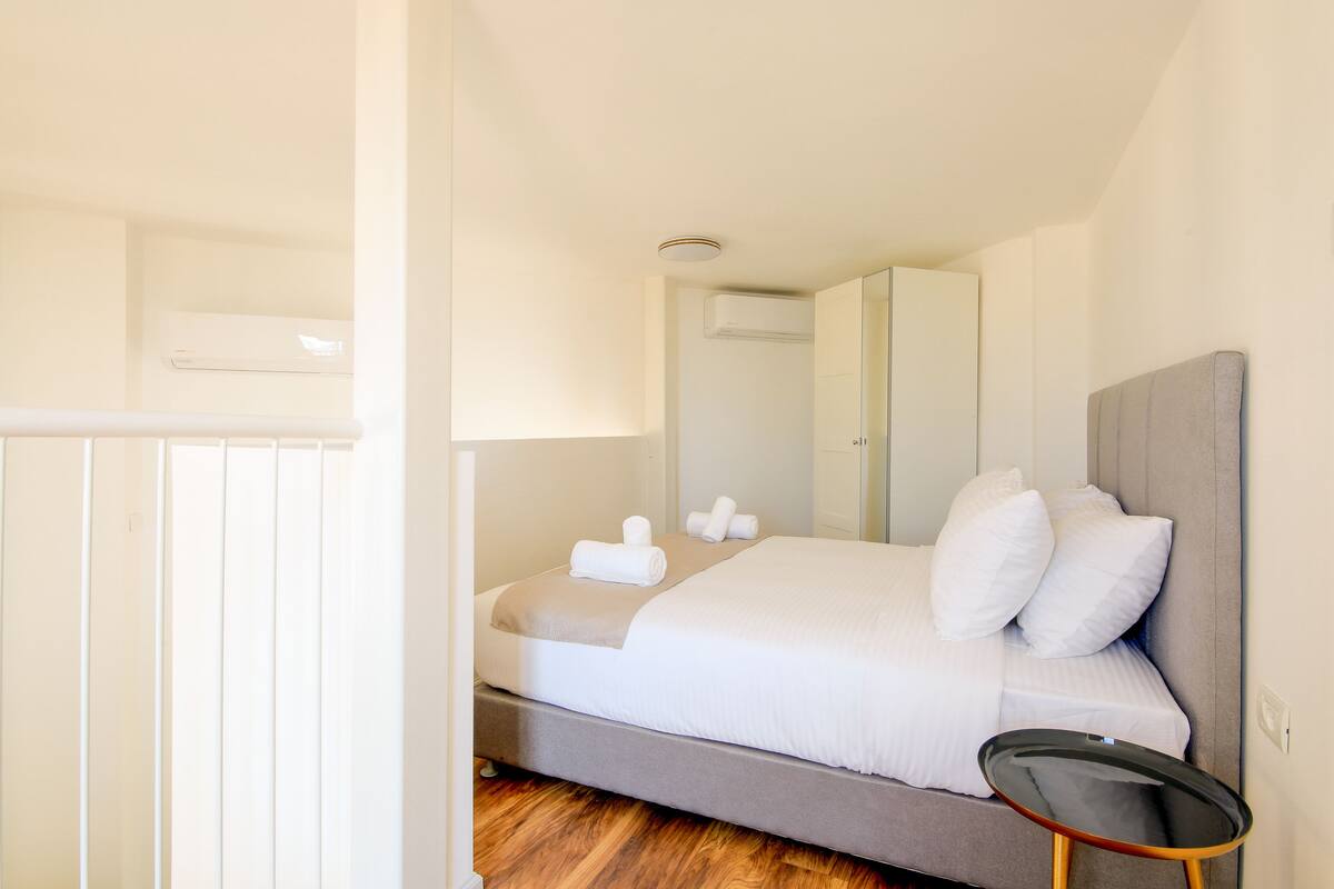 A modern hotel room with a bed, a bedside table, and a mirror.