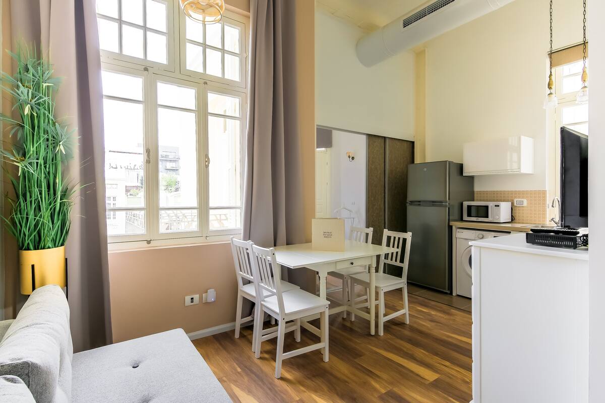 A compact kitchen with a dining table, chairs, a refrigerator, microwave, and a washing machine.