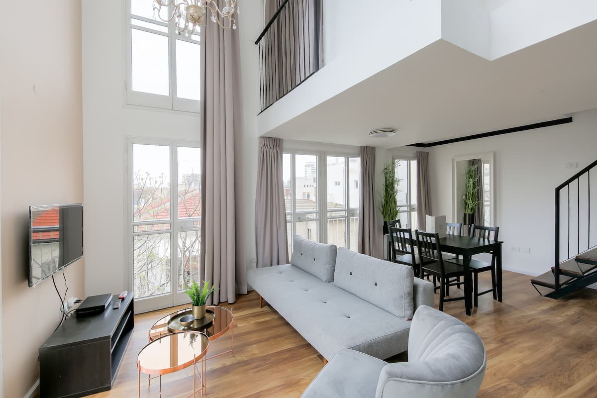 A modern living room with a grey sofa, a dining table with chairs, a TV, and a staircase.