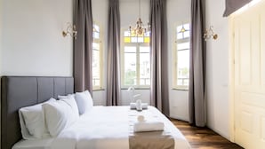 A neatly made bed with pillows and a blanket, a chandelier, and curtains on a window. - House of Palm (Tel Aviv)