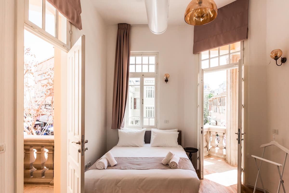 A hotel room with a bed, a window with curtains, a balcony, and a hanging light fixture.