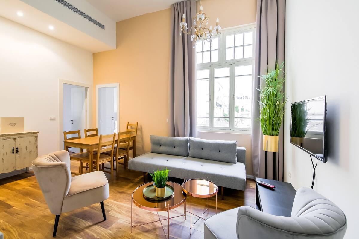 A modern living room with a sofa, two armchairs, a dining table, and a TV.