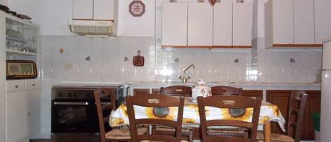 Una cocina con armarios blancos, una estufa y una mesa de comedor con sillas.