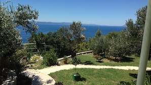 A garden with a pathway, a wheelbarrow with flowers, and a view of the sea.