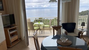 A balcony with a table and chairs, a television, and a view of the sea.