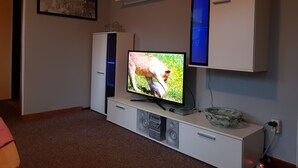 Ein Wohnzimmer mit einem Flachbildfernseher auf einer weißen Unterhaltungsecke, einem gerahmten Bild an der Wand und einem Regal darüber.