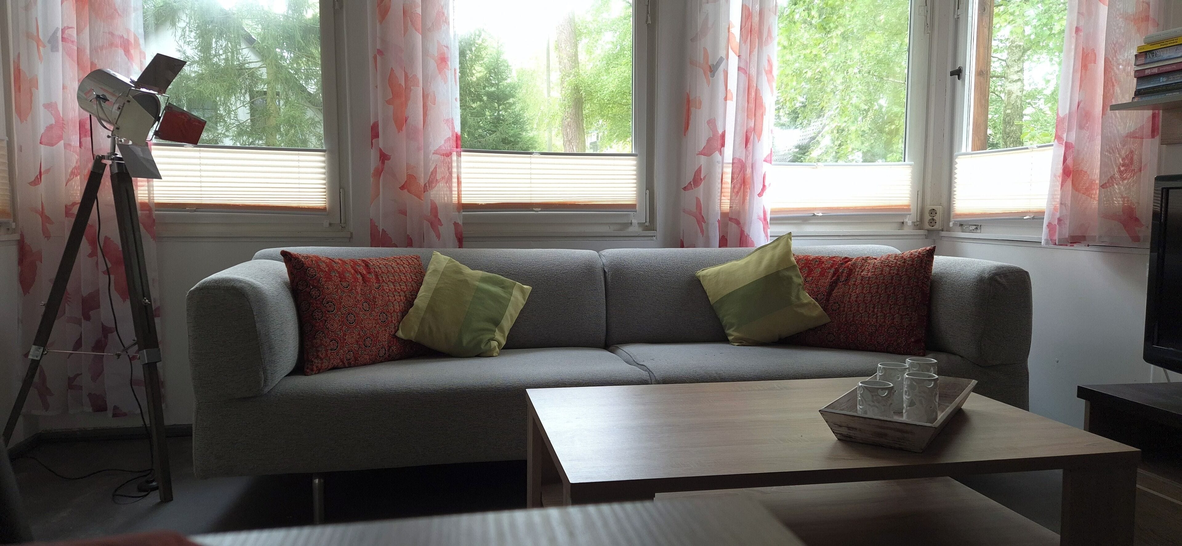 Un salon avec un canapé gris, deux coussins à motifs, une table basse en bois et un appareil photo fixé sur un trépied.