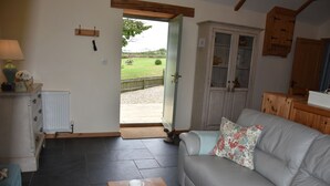 A cozy living room with a grey sofa, a wooden coffee table with a teapot and cups, and a view of a garden through an open door. - Rural Complex 7 Lux Cottages, Beech Cottage Sleeps 2, 1 well behaved dog allowed (Tregony)