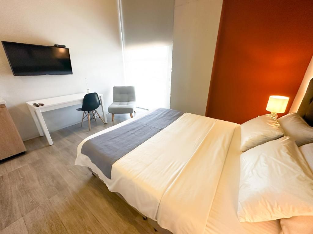 A hotel room with a bed, a desk, a chair, a TV, and a window.