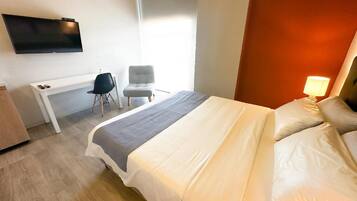 A hotel room with a bed, a desk, a chair, a TV, and a window.