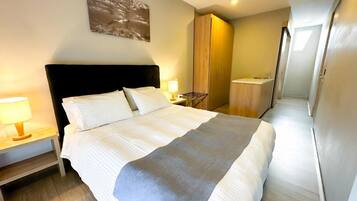Quarto de hotel com uma cama grande, mesa de cabeceira com abajur, guarda-roupa e banheiro com pia.