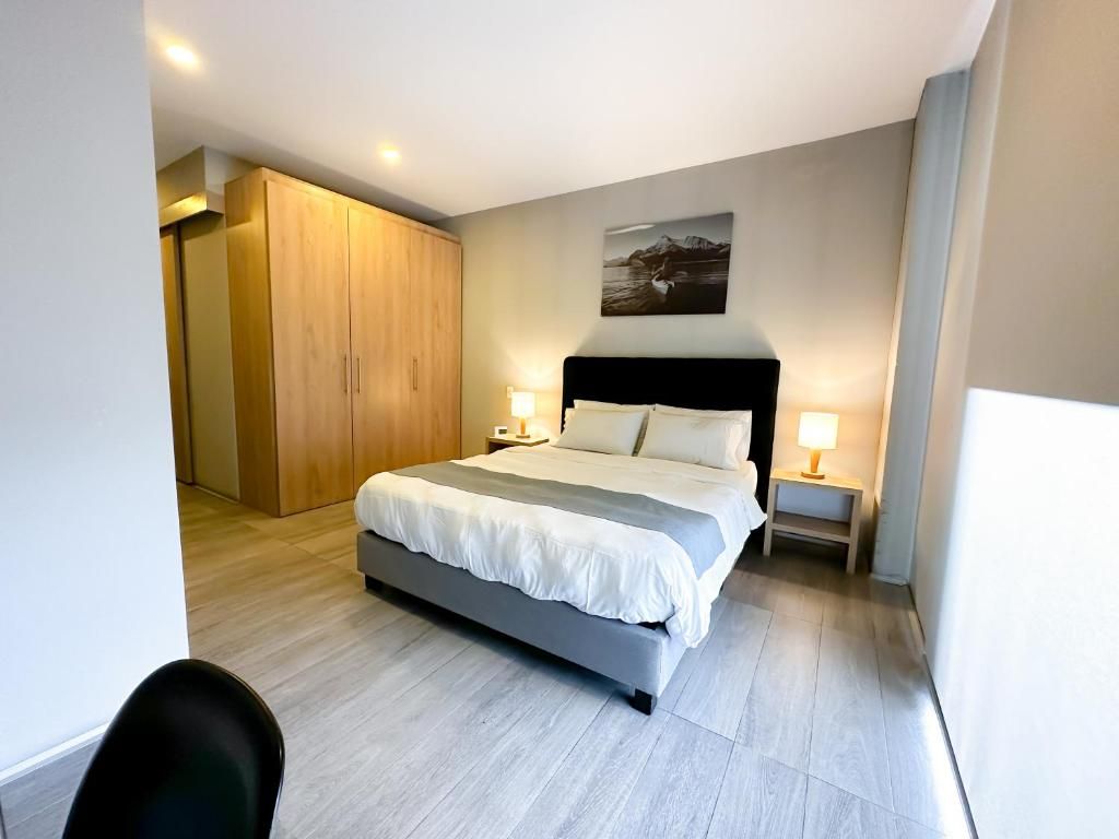 A modern hotel room with a large bed, bedside lamps, a wooden wardrobe, and a framed picture on the wall.