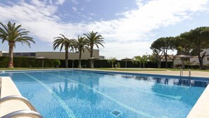 Una piscina cristalina con una escalera para entrar, rodeada de palmeras y un edificio al fondo.