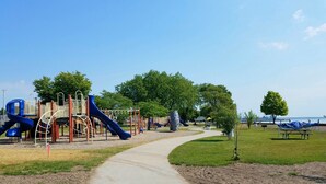Un parque infantil con toboganes y estructuras para escalar, un sendero para caminar y una zona de playa con sombrillas.