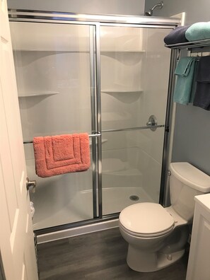 A bathroom with a glass-enclosed shower, a white toilet, and a towel rack with multiple towels.