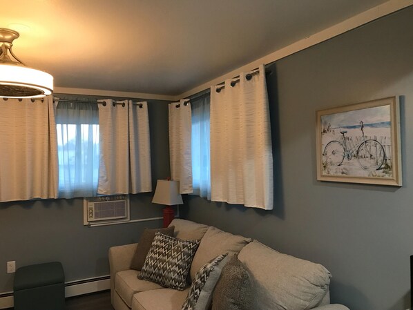 A living room with a sofa, a lamp, and a painting of a bicycle.