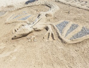 A sand sculpture of a dinosaur with a long neck and tail, surrounded by small pebbles.