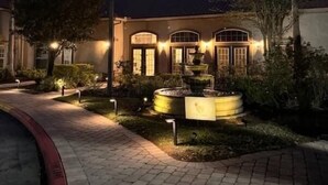 Un edificio bien iluminado con una fuente, un sendero pavimentado y ventanas de arco.