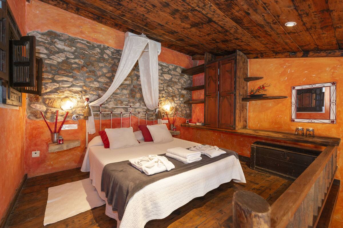 Quarto com parede de pedra, teto de madeira e cama com roupa de cama branca.