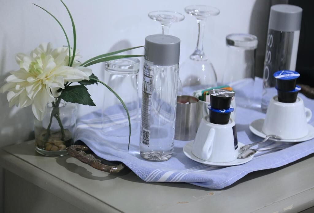 A table with a white flower, a clear bottle, a glass, and a white cup with a spoon.