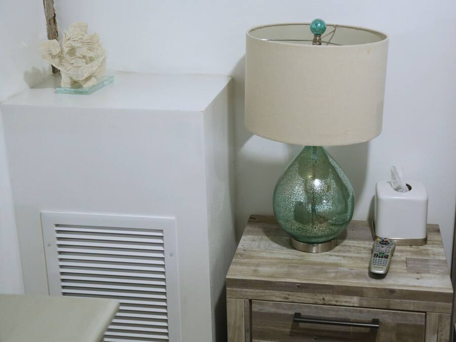 A bedside table with a green glass lamp, a tissue box, and a remote control.