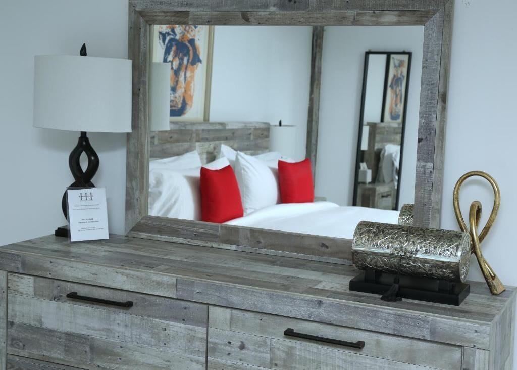 A bedroom with a wooden dresser, a mirror, a lamp, and a bed with red pillows.