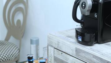 Une machine à café posée sur un meuble en bois doté d’une poignée, un panier rempli de bouteilles et un mur orné d’un motif circulaire.
