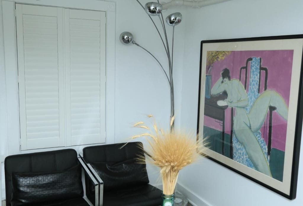 Ein Zimmer mit einer weißen Tür, einem schwarzen Stuhl, einer Vase mit Trockenpflanzen und einem gerahmten Gemälde an der Wand.