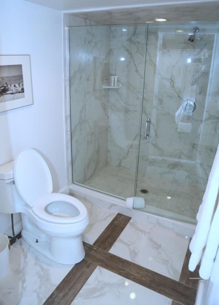 A bathroom with a glass-enclosed shower, a white toilet, and a marble floor.