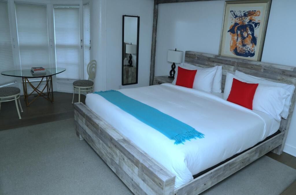 Ein Schlafzimmer mit einem hölzernen Bett, weißer Bettwäsche, einer blauen Decke und roten Kissen.