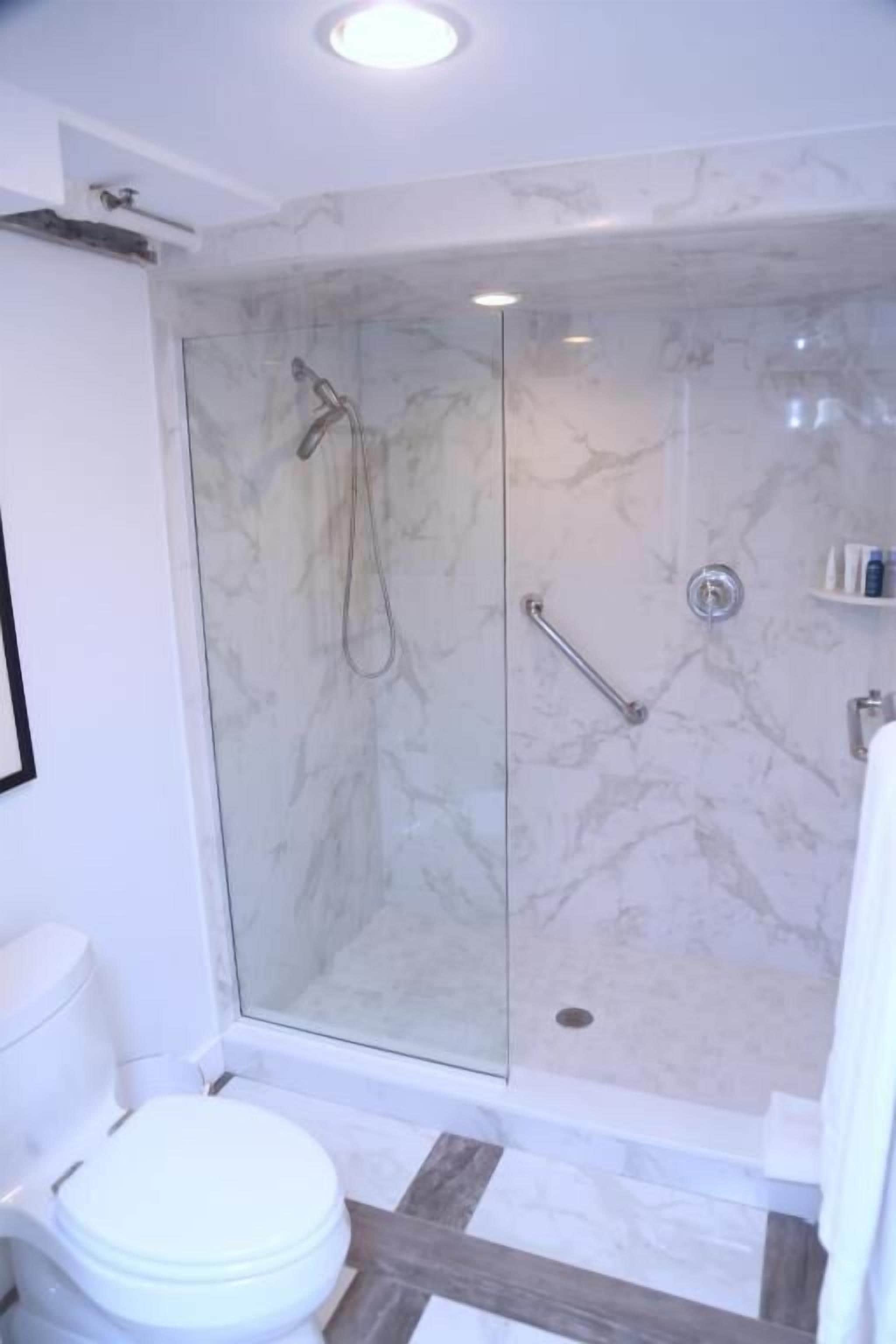 A bathroom with a glass-enclosed shower, a toilet, and a marble floor.
