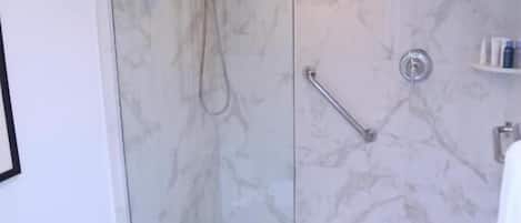 A bathroom with a glass-enclosed shower, a toilet, and a marble floor.