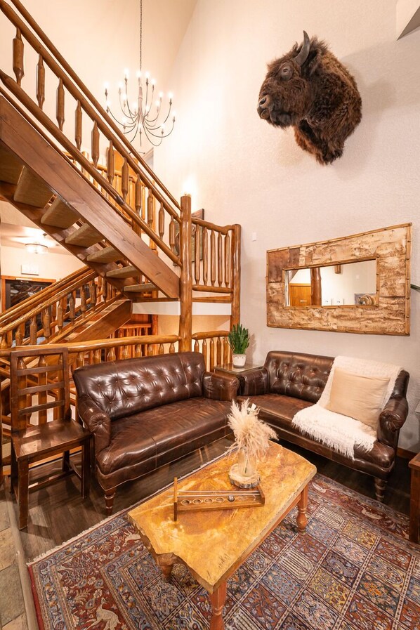 Un amplio salón con una escalera de madera, sofás de cuero, una mesa de centro y una cabeza de animal montada.