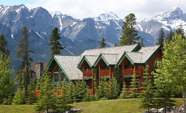 A lodge with a stone facade and green roof, surrounded by trees and mountains. - A Bear and Bison Inn (Canmore)