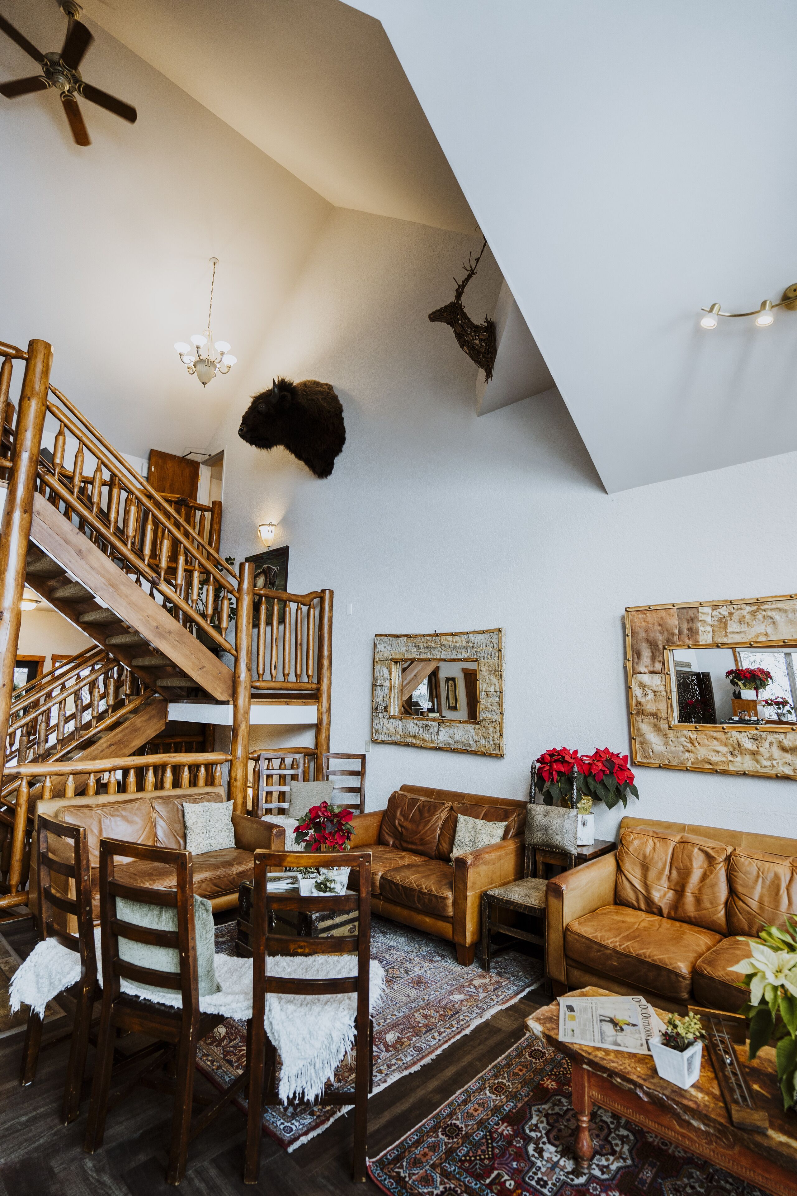 Amplia sala de estar con escalera de madera, muebles de cuero y detalles decorativos como un candelabro y una cabeza de animal montada en la pared.
