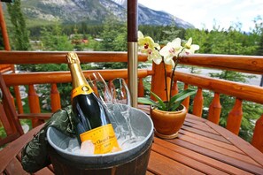 A wooden table with a bottle of champagne, glasses, and a potted orchid on a balcony with a mountain view. - A Bear and Bison Inn (Canmore)